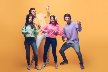 Mutlu arkadaşlar kulaklıkla müzik dinliyorlar ve sarı renkte dans ediyorlar.