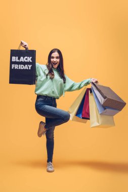 Heyecanlı kadın siyah cuma günü alışveriş torbalarıyla atlıyor, sarı renkte.