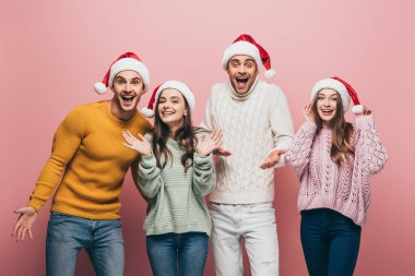Pembe kazak ve Noel Baba şapkası giyen heyecanlı arkadaşlar.