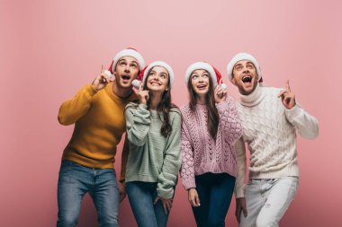 Süveter ve Noel Baba şapkalı mutlu arkadaşlar, pembe üzerinde izole edilmiş.