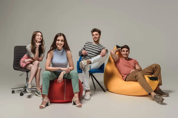 Amis Souriants Assis Sur Différentes Chaises Sur Gris — Photo