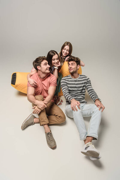 Счастливые друзья, сидящие вместе на шезлонге, на сером
