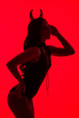 silueta smyslné ženy v kostýmu ďábla, izolovaná na červené