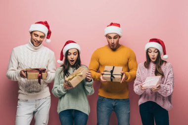 Noel Baba şapkalı sürpriz arkadaşlar ellerinde hediyeler, pembe renkte izole edilmiş.