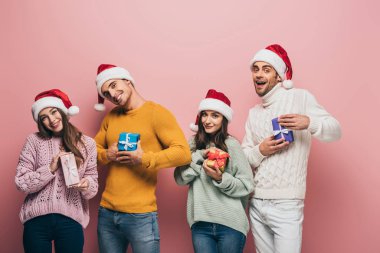 Noel Baba şapkalı mutlu arkadaşlar Noel hediyeleri taşıyorlar, pembe renkte izole edilmiş.
