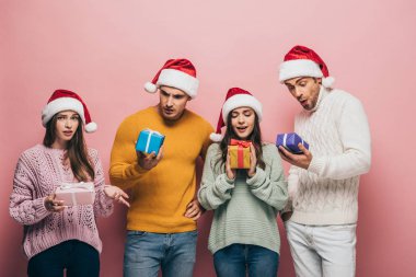 Noel Baba şapkalı sürpriz arkadaşlar ellerinde hediyeler, pembe renkte izole edilmiş.