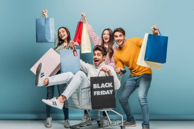 excited friends having fun with shopping bags in shopping cart on black friday, on blue clipart