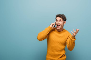 Yakışıklı, heyecanlı adam akıllı telefonla konuşuyor, mavi ile izole edilmiş.