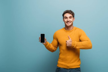 Mutlu adam parmakla görünüyor ve akıllı telefon boş ekran ile, mavi üzerinde izole
