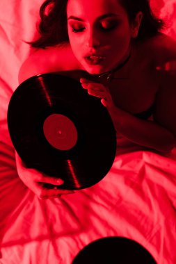 Yatakta oturan çekici seksi kadın. Kırmızı ışıkta plaklar var.
