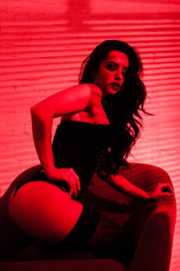 Güzel, tutkulu kadın kırmızı ışıkta vücut kıyafetiyle poz veriyor.