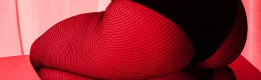 cropped view of sexy buttocks of girl in fishnet tights in red light, panoramic shot clipart