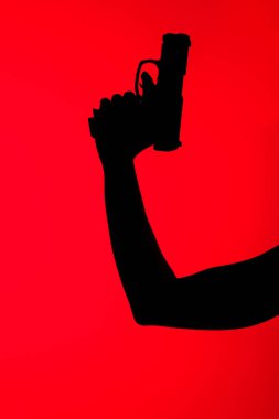 cropped view of silhouette of woman holding gun isolated on red clipart