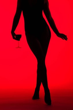 Kırmızıda izole edilmiş şarap kadehini tutan siyah siluet seksi kadın görüntüsü