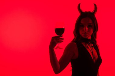 Şeytan kostümlü seksi bir kız silueti elinde şarap kadehi, kırmızı üzerine izole edilmiş.