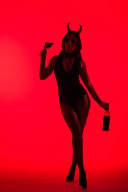silhouette of sexy girl in Devil costume holding glass and bottle of wine, isolated on red clipart