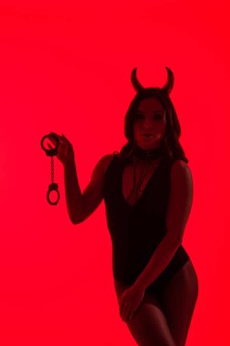 Şeytan kostümlü seksi bir kız silueti. Elinde kelepçe var. Kırmızıda izole edilmiş.
