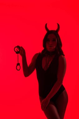 silhouette of sexy girl in Devil costume holding handcuffs, isolated on red clipart