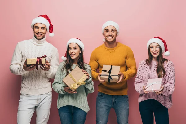 Amigos Sonrientes Sombreros Santa Celebración Regalos Navidad Aislados Rosa — Foto de Stock