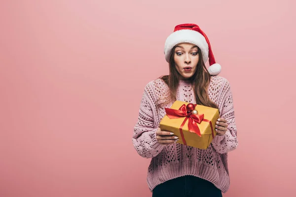 Здивована Жінка Светрі Капелюсі Санти Тримає Різдвяний Подарунок Ізольована Рожевому — стокове фото