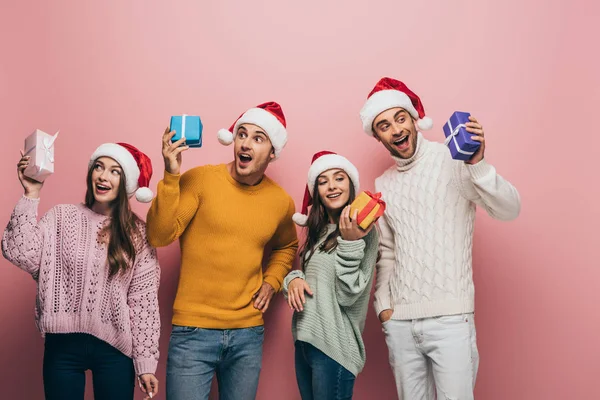 Excited Friends Santa Hats Holding Christmas Presents Isolated Pink — Stock Photo, Image