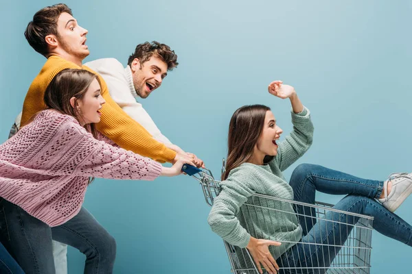 Excited Friends Having Fun Riding Girl Shopping Cart Isolated Blue — Stock Photo, Image