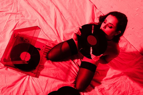 魅力的な魅惑的な女の子はベッドの上に座ってレコードで赤の光 — ストック写真