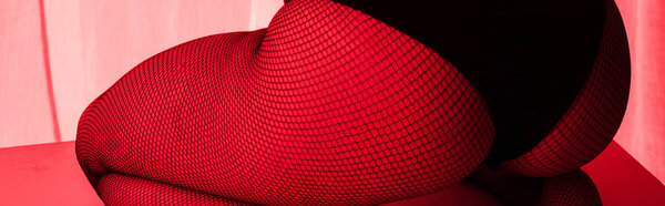 cropped view of sexy buttocks of girl in fishnet tights in red light, panoramic shot