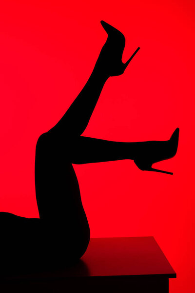 black silhouette of seductive woman in heels posing on table isolated on red