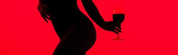 cropped view of black silhouette of sexy girl holding glass of wine isolated on red, panoramic shot