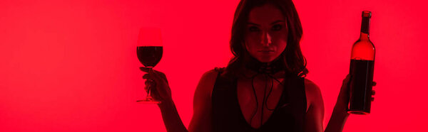 panoramic shot of attractive sexy woman holding bottle and glass of wine isolated on red