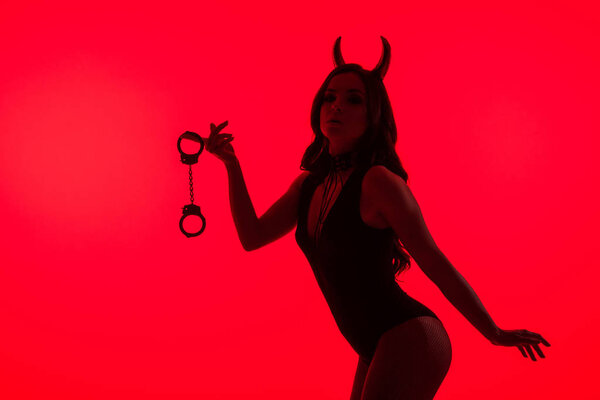Силуэт соблазнительной женщины в костюме Дьявола с наручниками, изолированными на красном
