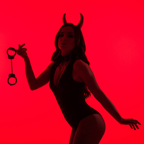 silhouette of passionate woman in Devil costume holding handcuffs, isolated on red