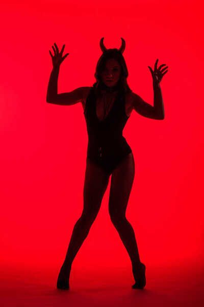 silhouette of beautiful young woman in Devil costume, isolated on red
