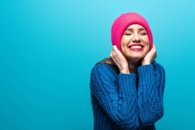 Çekici, pozitif bir kadın. Gözleri kapalı, örgü kazaklı, pembe şapkalı, mavi tenli.