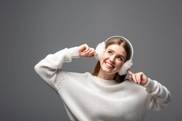 beautiful happy girl posing in white sweater and ear warmers, isolated on grey