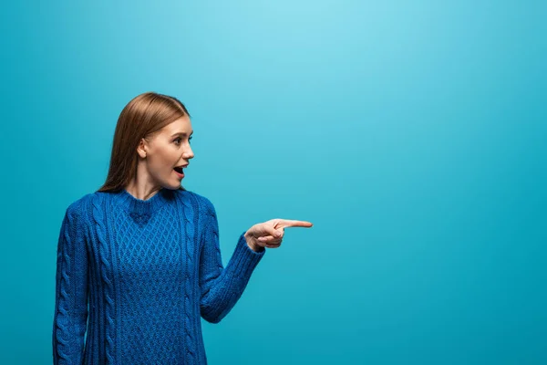 Vacker Upphetsad Kvinna Blå Stickad Tröja Pekar Något Isolerad Blå — Stockfoto