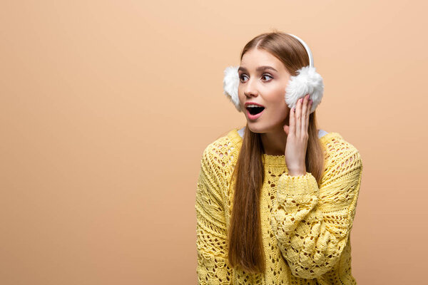 attractive excited woman in yellow sweater and earmuffs, isolated on beige