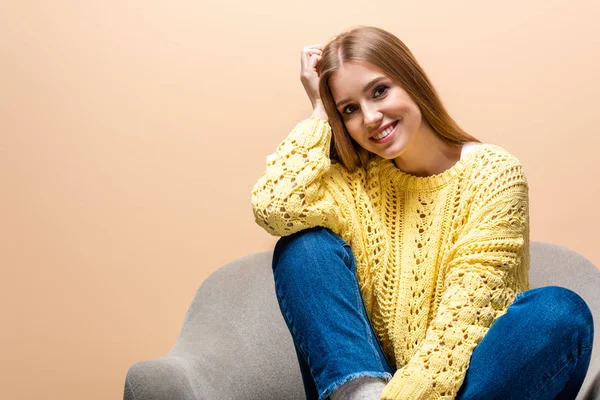 黄色のセーターを着た美しい幸せな女性がアームチェアに座ってベージュで隔離され — ストック写真