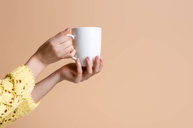 Sarı kazaklı bir kadının elinde kahve fincanı, bej rengi üzerinde izole edilmiş.