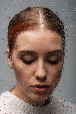 sad lonely woman on grey, beyond wet glass with drops  clipart