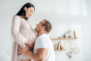 Mutlu yakışıklı koca yatak odasında hamile karısına sarılıyor. 