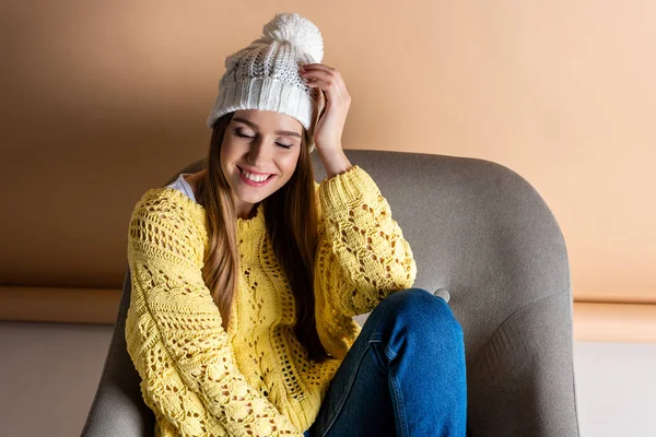 黄色のセーターを着た幸せな女性とベージュのアームチェアに座っている帽子 — ストック写真