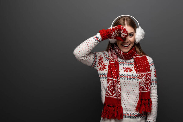 attractive happy woman in christmas sweater, scarf, mittens and earmuffs, isolated on grey