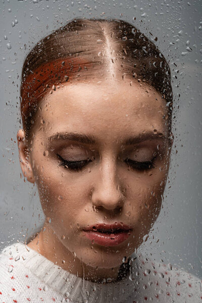 sad lonely woman on grey, beyond wet glass with drops 