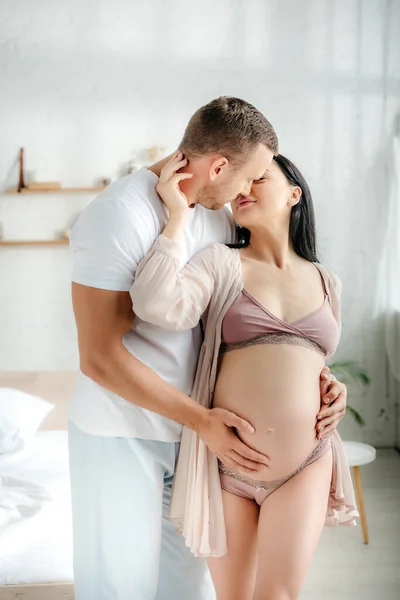 英俊的丈夫在卧室里拥抱和亲吻他怀孕的妻子 — 图库照片