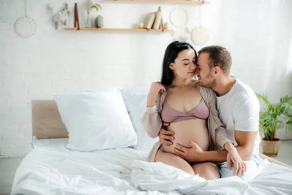 幸せな男は妊娠中の妻をベッドで抱きかかえて — ストック写真