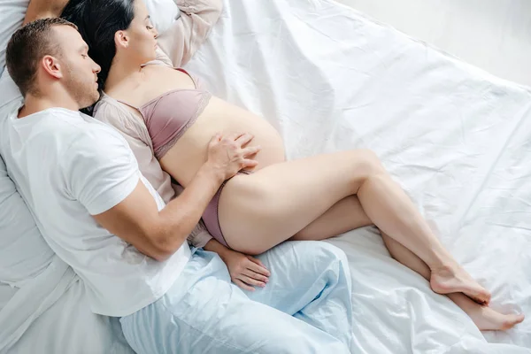 ベッドに横になって妊娠中の妻を抱きしめる夫の姿 — ストック写真