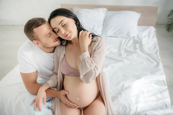 微笑的丈夫在床上拥抱和亲吻他怀孕的妻子 — 图库照片