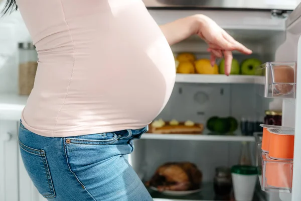 Vista Ritagliata Della Donna Incinta Che Punta Nel Frigorifero Aperto — Foto Stock